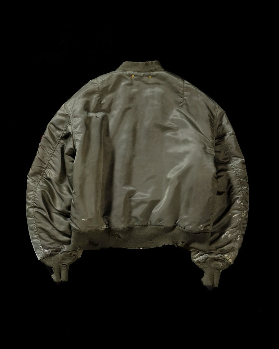 忠実なディテールを保ちながら、シルエットを現代的に整えたMA-1ジャケット。加工によりヴィンテージの風合いを再現した一着です。肉厚でミリタリーらしいツイル生地を使用し、打ち込みの密度や肌触りまでビンテージMA-1に近い仕上がりに。さらに、ダートペイントや特殊吹き付け、ダメージ加工を重ね、洗いをかけて染料を自然に剥がすことで、深みのある表情を生み出しています。カラーはオリーブ。
