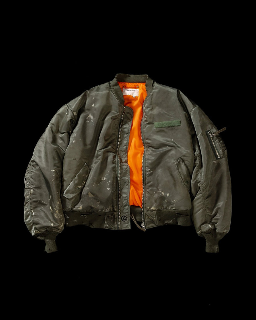 忠実なディテールを保ちながら、シルエットを現代的に整えたMA-1ジャケット。加工によりヴィンテージの風合いを再現した一着です。肉厚でミリタリーらしいツイル生地を使用し、打ち込みの密度や肌触りまでビンテージMA-1に近い仕上がりに。さらに、ダートペイントや特殊吹き付け、ダメージ加工を重ね、洗いをかけて染料を自然に剥がすことで、深みのある表情を生み出しています。カラーはオリーブ。